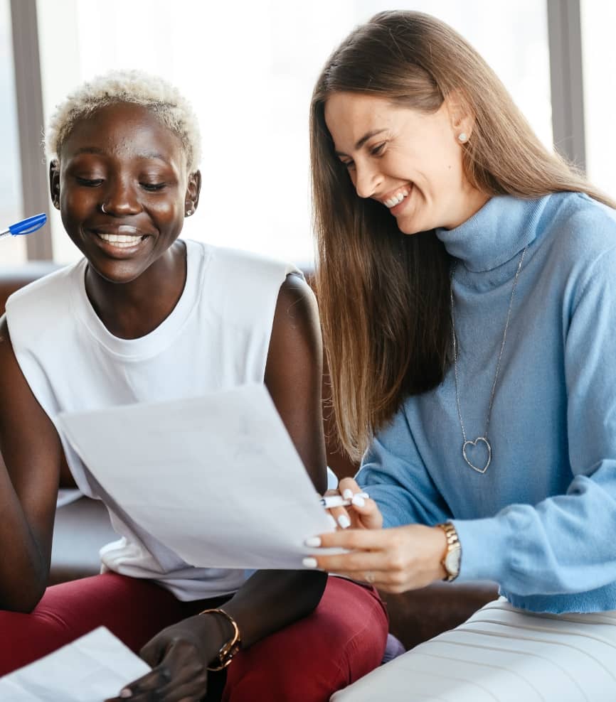 Two women smiling whilst looking at a piece of paper