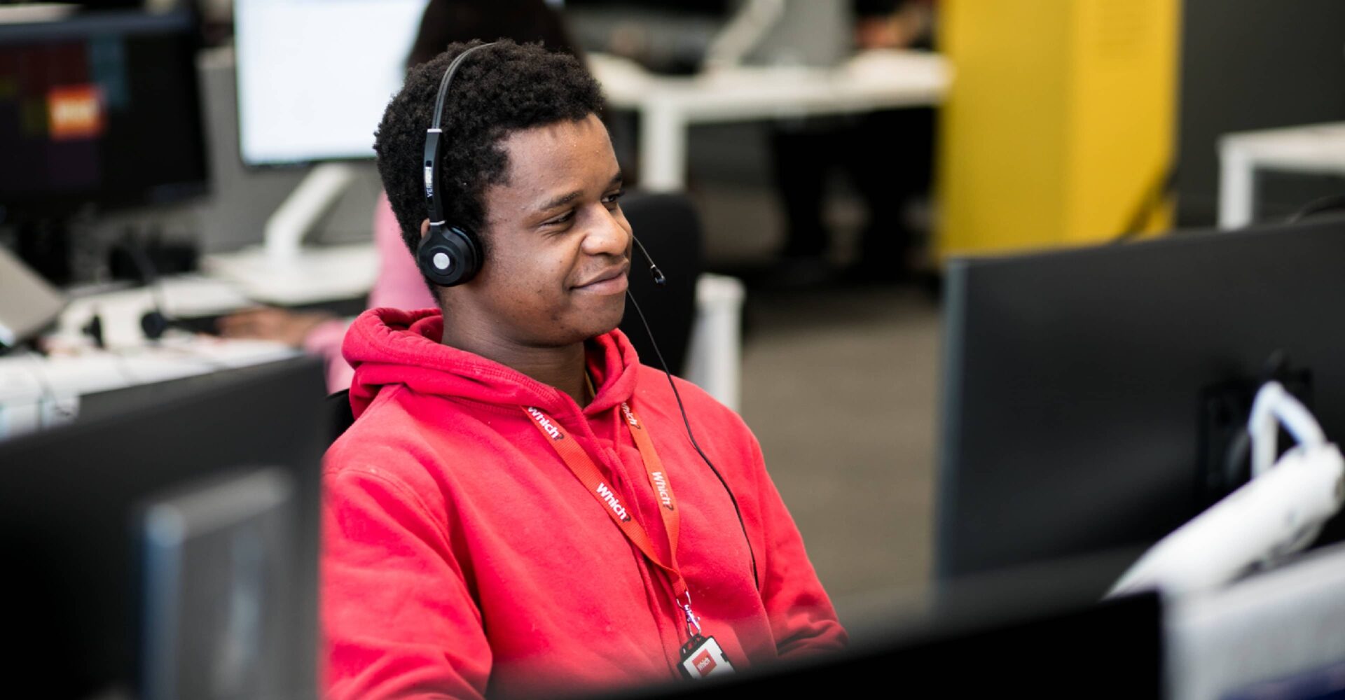 Man sat at a computer desk with headphones and a red hooded jumper